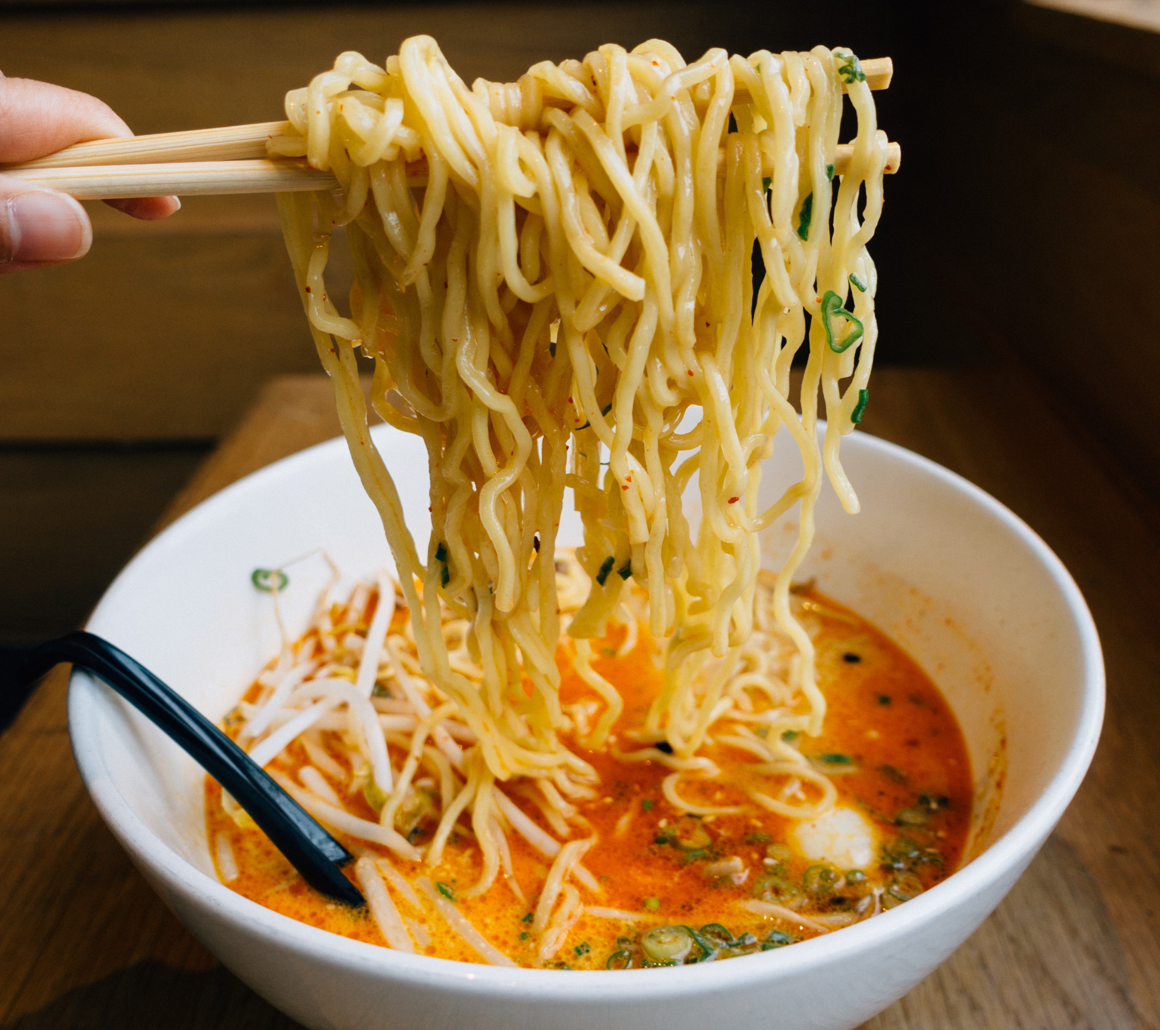 Chopsticks full of ramen noodles in a bowl of spicy soup.